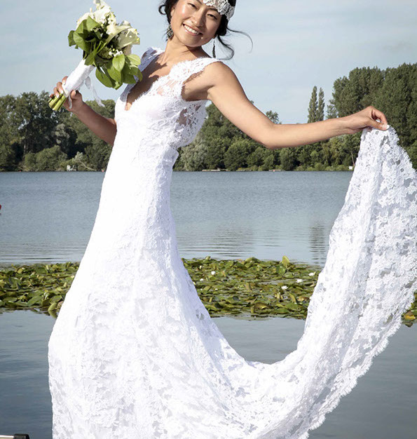 LA MARI2E EST EN POSE LAT2RALE AVEC UN BOUQUET DANS SA MAIN DROITE ET SA ROBE REHAUSS2E PAR SA MAIN GAUCHE SUR UN EMBARQUADERE